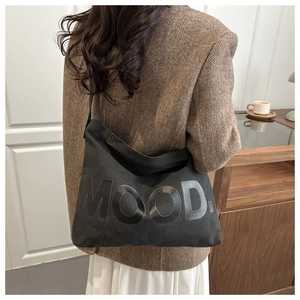 Dettaglio di una borsa a tracolla in tela nera con scritta MOOD su un blazer a spina di pesce
