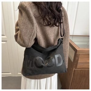 Dettaglio della borsa tote in tela nera con scritta MOOD indossata su una giacca marrone