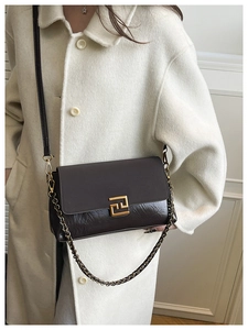 Détail du sac bandoulière en cuir marron avec boucle dorée sur un manteau beige élégant