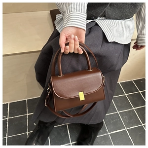 Detail of dark brown leather crossbody bag with golden metal buckle held by model