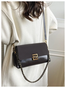 Détail d'un sac bandoulière marron foncé avec boucle dorée et texture cuir sur un mannequin