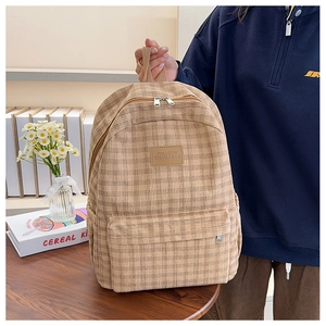 Detail of khaki corduroy plaid backpack with leather logo on a wooden table