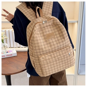 Brown plaid corduroy backpack with front pocket and logo patch worn in lifestyle setting