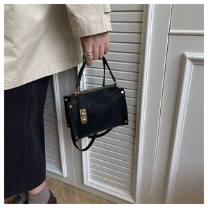 Dettaglio della borsa minimalista in pelle nera opaca con hardware dorato e chiusura a vite