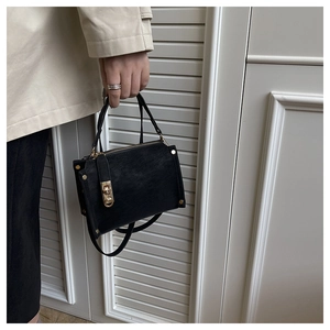 Macro detail of textured black leather handbag featuring gold metal clasp and zippers