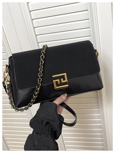 Détail d'un sac bandoulière noir en cuir avec chaîne dorée et fermoir métallique rectangulaire
