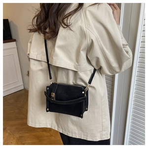 Detail of a chic black suede crossbody bag with gold hardware on a beige trench coat