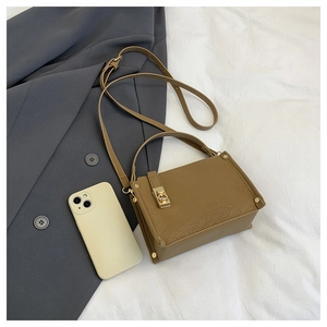 Detail of a brown leather square bag featuring a gold rotating lock and rivet accents