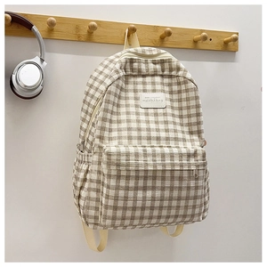 Detail of plaid canvas backpack with front zipper pocket and leather logo patch on hook