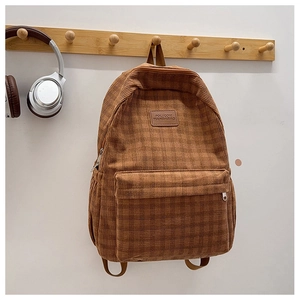 Detail view of brown corduroy backpack with retro plaid texture hanging on a wooden hook