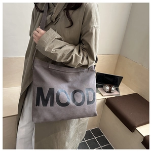 Borsa a tracolla in tela grigia con stampa MOOD indossata sopra un trench kaki classico