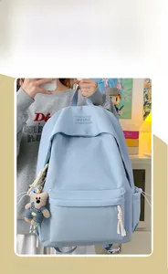 Detail of light blue school backpack with a cute teddy bear plush charm and front pocket