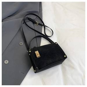 Detail view of black textured crossbody bag with gold square buckle and metal rivets