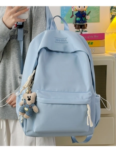 Detail of light blue nylon backpack featuring a logo imprint and a cute bear plush pendant