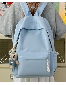 Close-up of light blue backpack with XINFEIDA logo and a cute teddy bear charm