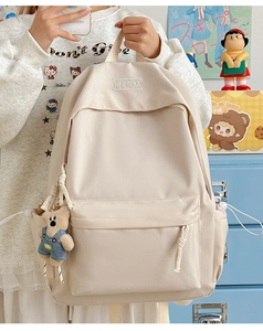 Detail of a beige minimalist nylon backpack featuring a bear charm and brand embroidery