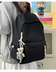 Detail of black nylon backpack featuring woven rope pulls and cute plush bear charm decoration