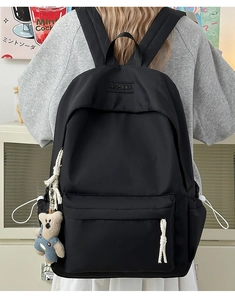 Detail of minimalist black nylon backpack with plush bear charm and white woven zipper pull