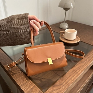 Caramel brown leather crossbody bag with gold buckle and top handle in a cozy cafe setting