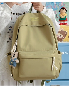 Detail of khaki nylon backpack featuring drawstring side pockets and a cute bear charm