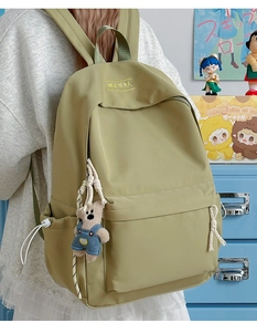 Detail of light olive nylon backpack featuring XINFEIDA embroidery and a cute bear charm