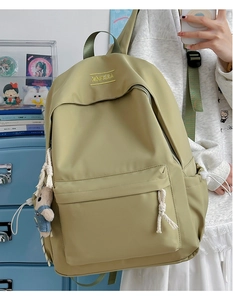 Detail of light olive green backpack featuring XINFEIDA embroidery and cute bear charm