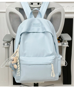 Close-up of light blue backpack with XINFEIDA embroidery and cute teddy bear charm