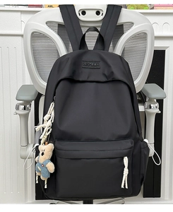Detail of black nylon backpack featuring XNFEIDA embossed logo and a cute teddy bear charm