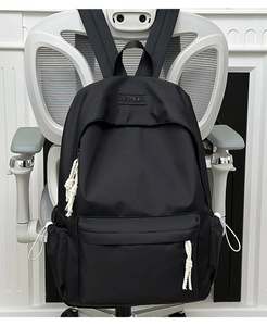Detail of minimalist black backpack featuring embossed logo and woven zipper pull knots