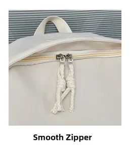 Macro detail of smooth dual metal zippers and woven pulls on a cream nylon backpack