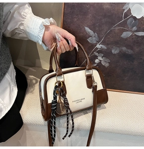 Detail of cream and brown boston bag with a unique tennis racket charm and text logo