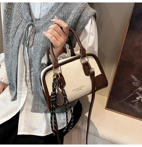 Detail of cream leather boston bag with brown handles and tennis racket charm