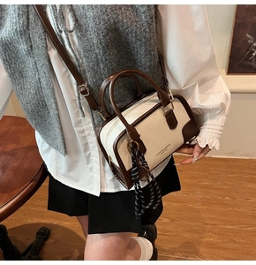 Detail of beige Boston bag with brown trim and woven charm accessory on a model