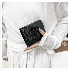 Detail of a black patent leather envelope clutch bag with crocodile texture held by hand