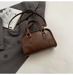 Top-down view of dark brown leather shoulder bag on a grey suit with gold buckles