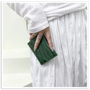 Close-up of a small dark green glossy patent leather envelope bag with crocodile pattern