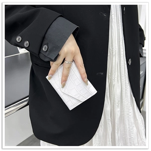 Close-up of white crocodile texture clutch bag held by a model in a black suit