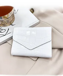 Detalle de cartera sobre blanca con relieve de cocodrilo y costuras sobre tela beige