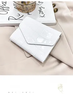 Detalle de un bolso de sobre blanco con textura de cocodrilo sobre fondo beige