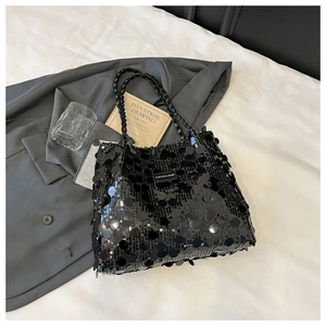 Detail of black sequin tote bag with woven handles and fashion label on white fabric