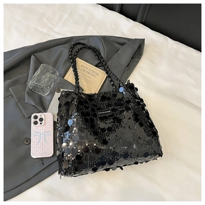 Detail of black sequin tote bag with woven handles and fashion label on soft fabric