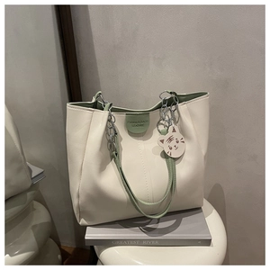 Detail of cream tote bag with green accents, metal chain strap and cute animal charm