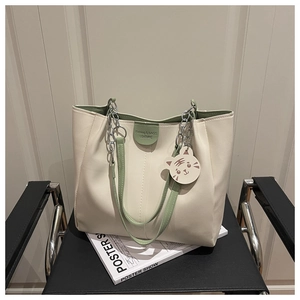 Detail of cream tote bag with green handles and cute tiger charm on a black chair