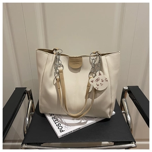 Detail of cream tote bag with silver chain, leather logo patch and tiger charm on a chair
