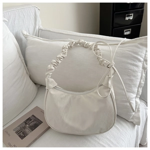 Detail of a beige half-moon hobo bag with a ruched cloud strap and bow accents