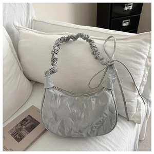 Detail of silver pleated crescent bag with metallic texture and bowknot on white sofa