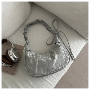 Detail of silver pleated dumpling bag with scrunchie strap and ribbons on a sofa