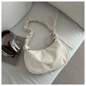 Detail shot of a cream crescent shoulder bag with pleated texture and stylish wide strap