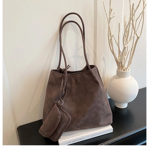 Détail du sac cabas en daim marron avec pochette zippée sur un fond minimaliste clair