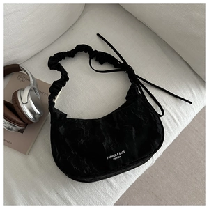 Close-up of black pleated crescent bag with wide shoulder strap on a beige fabric surface